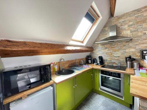 Elle comprend une petite cuisine avec des placards verts et une fenêtre. dans l'établissement Les combles de l Aure Grand studio cosy confortable classé 3 étoiles centre Bayeux 2 mn à pied cathédrale proche plages du débarquement, à Bayeux