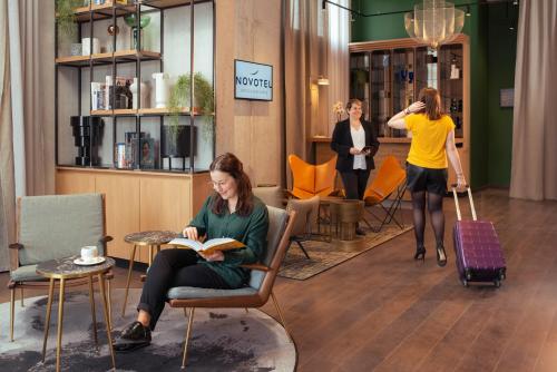 a woman sitting in a chair reading a book in a lobby at Novotel Annemasse Centre - Porte de Genève in Annemasse