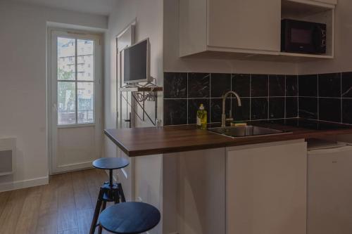 une cuisine avec un évier et un comptoir avec deux tabourets dans l'établissement Studio La Dent du Chat, à Chambéry