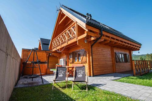 a wooden house with two chairs in front of it at Domki Gorczański Zakątek - Jacuzzi in Nowy Targ