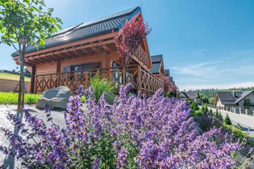 a log cabin with purple flowers in front of it at Domki Gorczański Zakątek - Jacuzzi in Nowy Targ