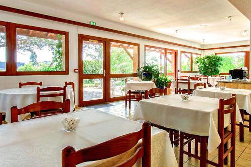 un restaurant avec des tables et des chaises blanches et des fenêtres dans l'établissement Brit Hotel Confort Pau Lons, à Lons