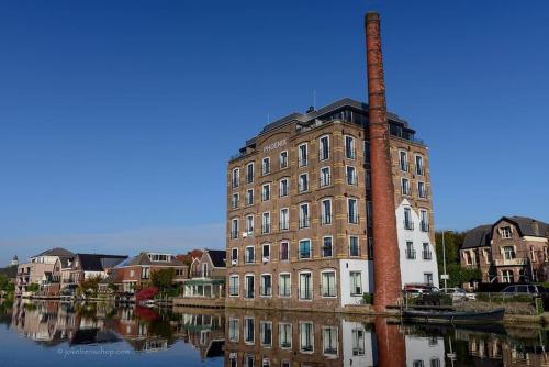 an old brick building with a chimney on the water at Waterval Wellness-suite met Sauna! in Bodegraven