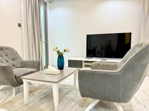 a living room with a tv and two chairs and a table at Al Safwa One in Al Ḩadd
