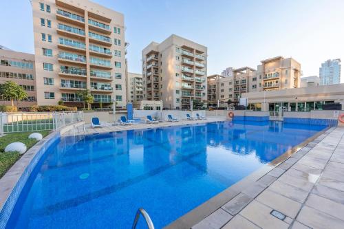 a large swimming pool with chairs and buildings at Charming 1BR in The Greens, Near Metro in Dubai