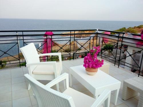 a balcony with white chairs and a table with pink flowers at Porto Skala Village Hotel in Skala Kefalonias