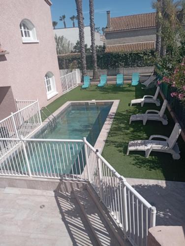 - une piscine avec des chaises longues et des chaises à côté d'un bâtiment dans l'établissement Villa Familiale Valras-plage avec Piscine Spa Sport, à Valras-Plage