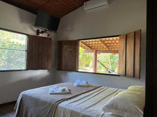 a bedroom with two towels on a bed with two windows at Pousada Rio das Almas in Pirenópolis