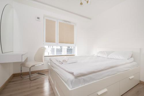 a white bedroom with a bed and a chair at Widzewska Deluxe Apartment by BookingHost in Łódź