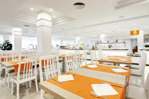 a restaurant with wooden tables and white chairs at Grupotel Mar de Menorca in Es Canutells