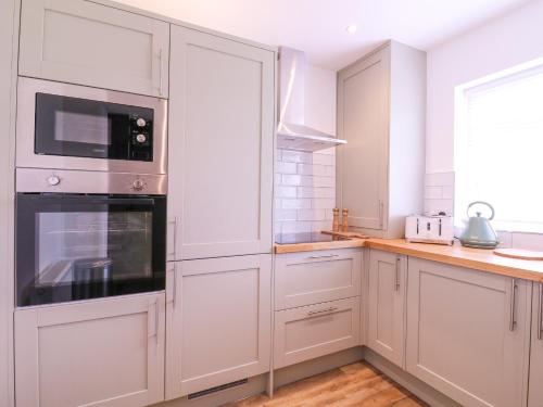 a white kitchen with white cabinets and a microwave at The Farmhouse in Clacton-on-Sea