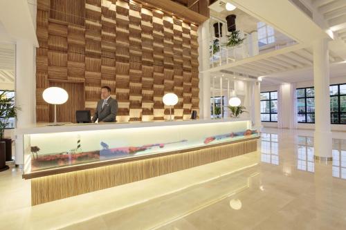 a man standing at a reception desk in a lobby at Grupotel Mar de Menorca in Es Canutells