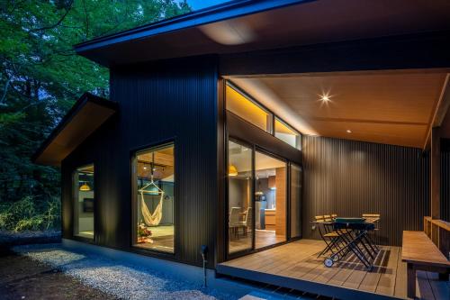 a glass house with a patio and a table on a deck at 森の宿り 時庵 まるやま in Nasu