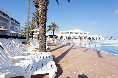 a row of white lounge chairs next to a swimming pool at Grupotel Mar de Menorca in Es Canutells