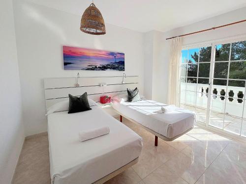 a white bedroom with two beds and a window at INIBIZA VILLAS - Villa Oasis in Sant Jordi