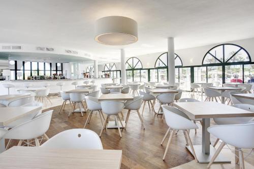 a restaurant with white tables and chairs and windows at Grupotel Mar de Menorca in Es Canutells