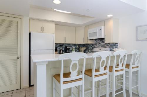 a kitchen with white cabinets and white bar stools at Shearin by Bryant Real Estate in Wrightsville Beach
