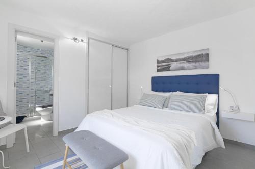 a white bedroom with a blue bed and a chair at La Casita Del Mar in Caleta de Caballo