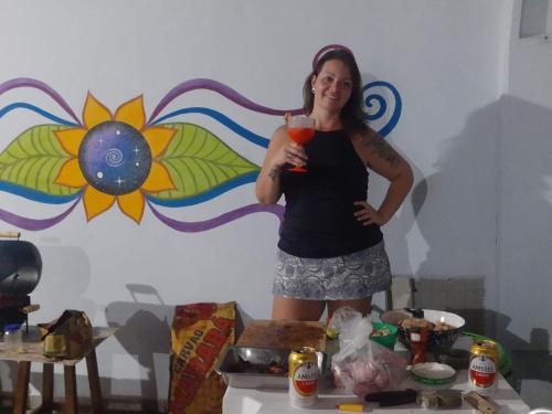 a woman holding a drink in front of a wall at Quarto para mulheres in Ubatuba