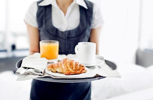 a waitress holding a tray with a plate of food and orange juice at Luxury Suite Koksijde 310 - Adults only in Koksijde