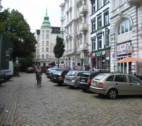 a person riding a bike down a street with parked cars at Altan Hotel in Hamburg