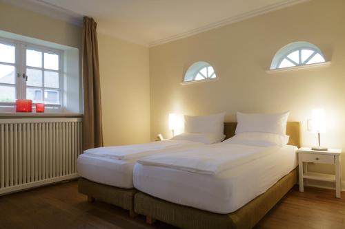 a bedroom with a large white bed with two windows at Hotel Aarnhoog in Keitum