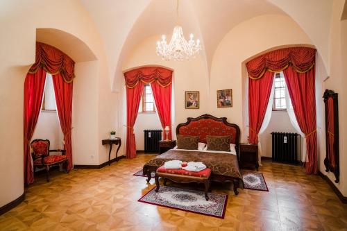 a bedroom with a bed and red curtains and a chandelier at Galicia Nueva, castle hotel in Lučenec