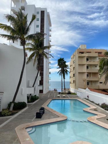 a swimming pool with palm trees next to a building at Marina del Sol Resort - beautiful 2 bdrm Sleeps 8 -Ocean front in Mazatlán