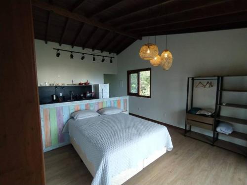 a bedroom with a white bed and a kitchen at Studio Ametista na praia do Silveira em Garopaba in Garopaba