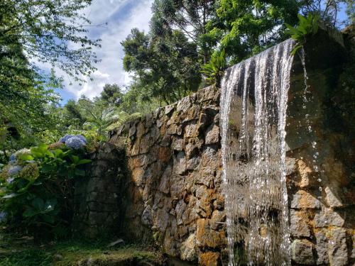 a waterfall on a stone wall in a garden at Sítio em Lumiar com piscina natural, sauna, churrasqueira e lareira in Nova Friburgo