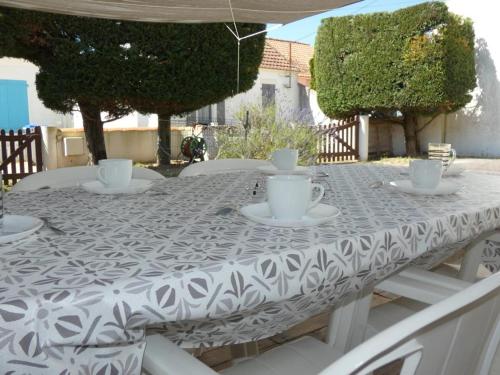 une table blanche avec des tasses et des soucoupes sur elle dans l'établissement Maison de vacances à Notre-Dame-de-Monts, proche plage, jardin, 6 pers, animaux permis - FR-1-540-283, à Notre-Dame-de-Monts