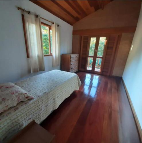 a bedroom with a bed and wooden floors and windows at Recanto do Sol in Bocaina de Minas