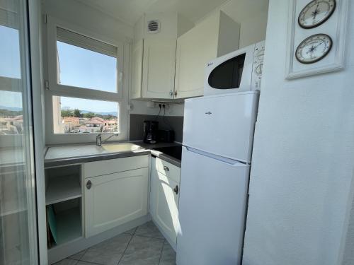 une cuisine avec un réfrigérateur blanc et une fenêtre dans l'établissement Studio lumineux face mer avec terrasse et parking, proche port et commerces, 4P - FR-1-799-31, au Barcarès