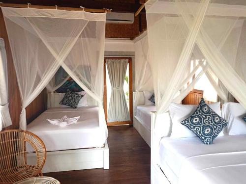 a bedroom with two white beds with curtains at Bintang Tiga Bungalows Gili Air in Gili Air