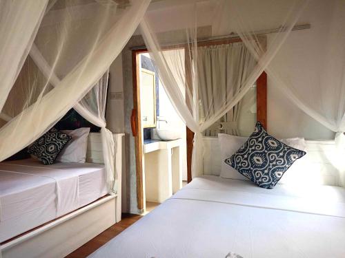 a bedroom with two beds with curtains and a window at Bintang Tiga Bungalows Gili Air in Gili Air