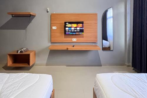 a bedroom with two beds and a tv on the wall at RedDoorz Plus at New Favour Hotel Gunung Dempo in Bumiagung