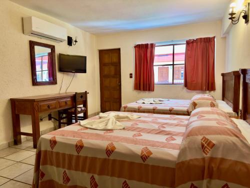 a bedroom with two beds and a desk and a television at Hotel Hacienda María Eugenia Acapulco in Acapulco