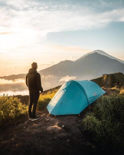 a person standing next to a tent on a mountain at Mount Batur Sunrise and Sunset Camping in Bangli