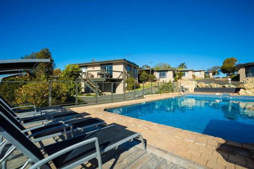 a swimming pool with lounge chairs next to a house at Eagle Heights Holiday Units in Eden