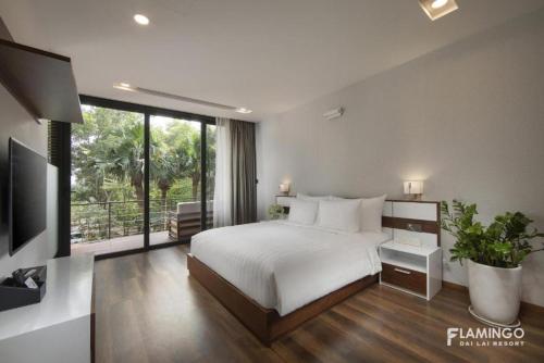 a bedroom with a white bed and a large window at Flamingo Resort Dai Lai in Ngọc Quang