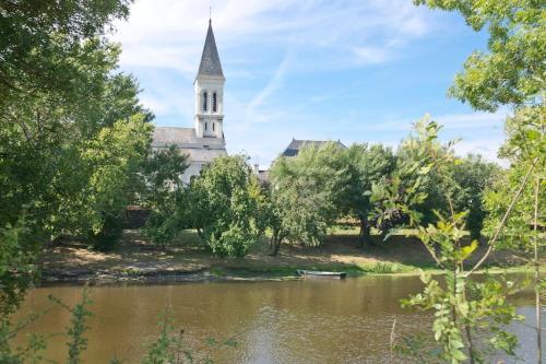 a church with a steeple and a river and trees at Entre Loire et Vignes in Juigné-sur-Loire