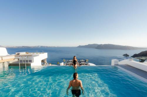 a man and a woman standing in a swimming pool overlooking the ocean at La Perla Villas and Suites - Adults Only in Oia