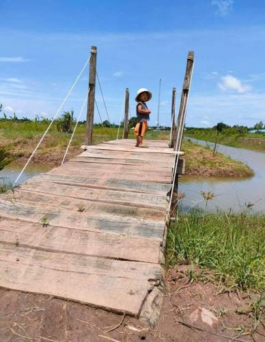 a person walking across a wooden bridge with an umbrella at Khu nghỉ dưỡng sinh thái Apsara Sóc Trăng in Ấp Vĩnh Hưng