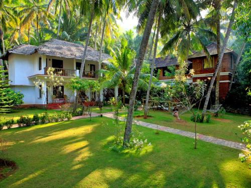 a house with palm trees in front of a yard at Abad Harmonia Ayurvedic Beach Resort in Kovalam