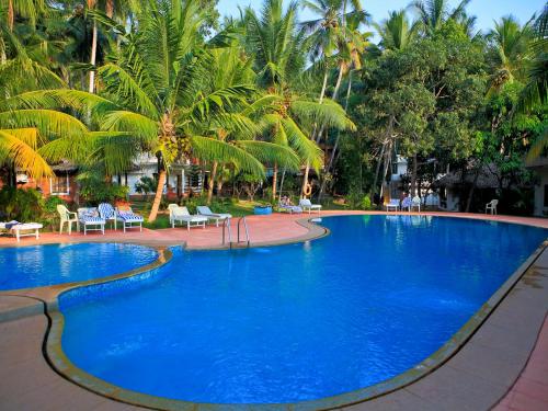 a large blue swimming pool with palm trees in the background at Abad Harmonia Ayurvedic Beach Resort in Kovalam