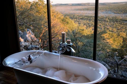 a bath tub in front of a window with a view at Little Ongava in Okaukuejo