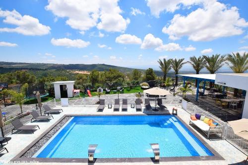a large swimming pool with chairs and a patio at אחוזת מיקונוס - וילה יוונית מושלמת עם בריכה מחוממת in Yarka