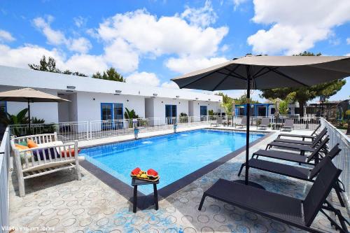 a swimming pool with two chairs and an umbrella at אחוזת מיקונוס - וילה יוונית מושלמת עם בריכה מחוממת in Yarka