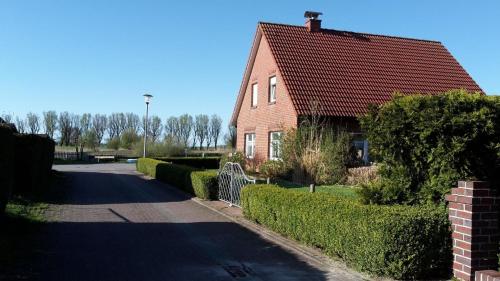 una casa in mattoni con tetto rosso su una strada di Freistehendes Haus mit großem, eingezäunten Garten, Sauna, Kamin a Krummhörn