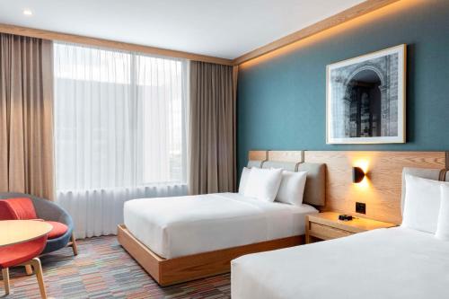 a hotel room with two beds and a chair and a table at Hilton Garden Inn Guadalajara Airport in Guadalajara